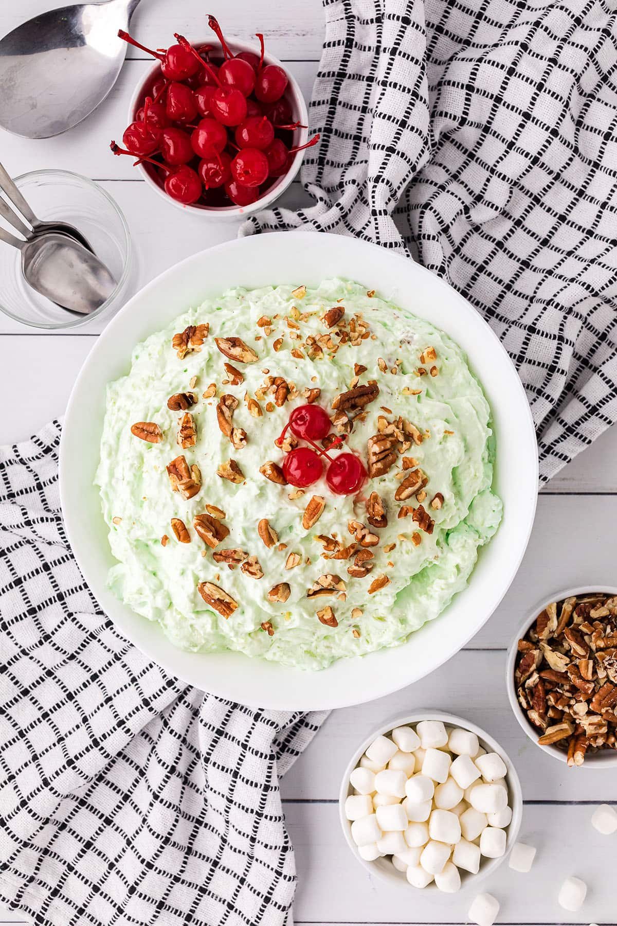 pistachio salad with chopped nuts and cherries on top in a white bowl sitting on a black and white towel with chopped nuts and cherries on top