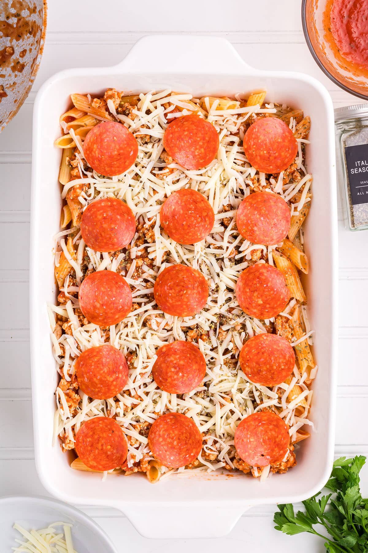 a baking dish with cooked pasta, ground chicken in red sauce with shredded cheese and pepperoni