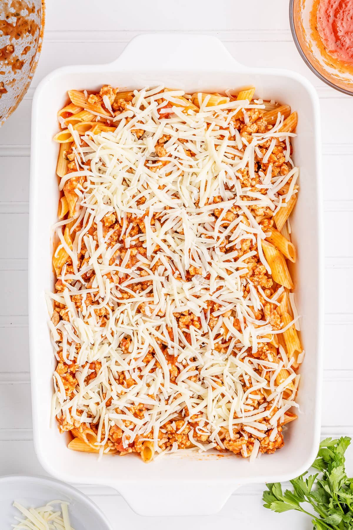 a baking dish with cooked pasta, ground chicken in red sauce with shredded cheese