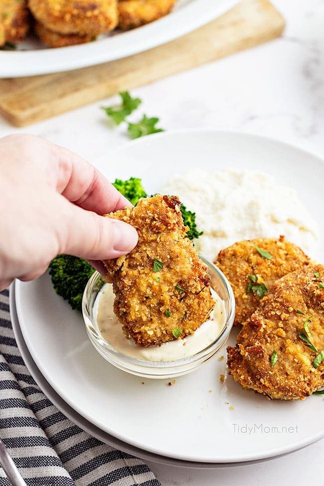 woman's hand dipping a crispy pork medallion in sauce