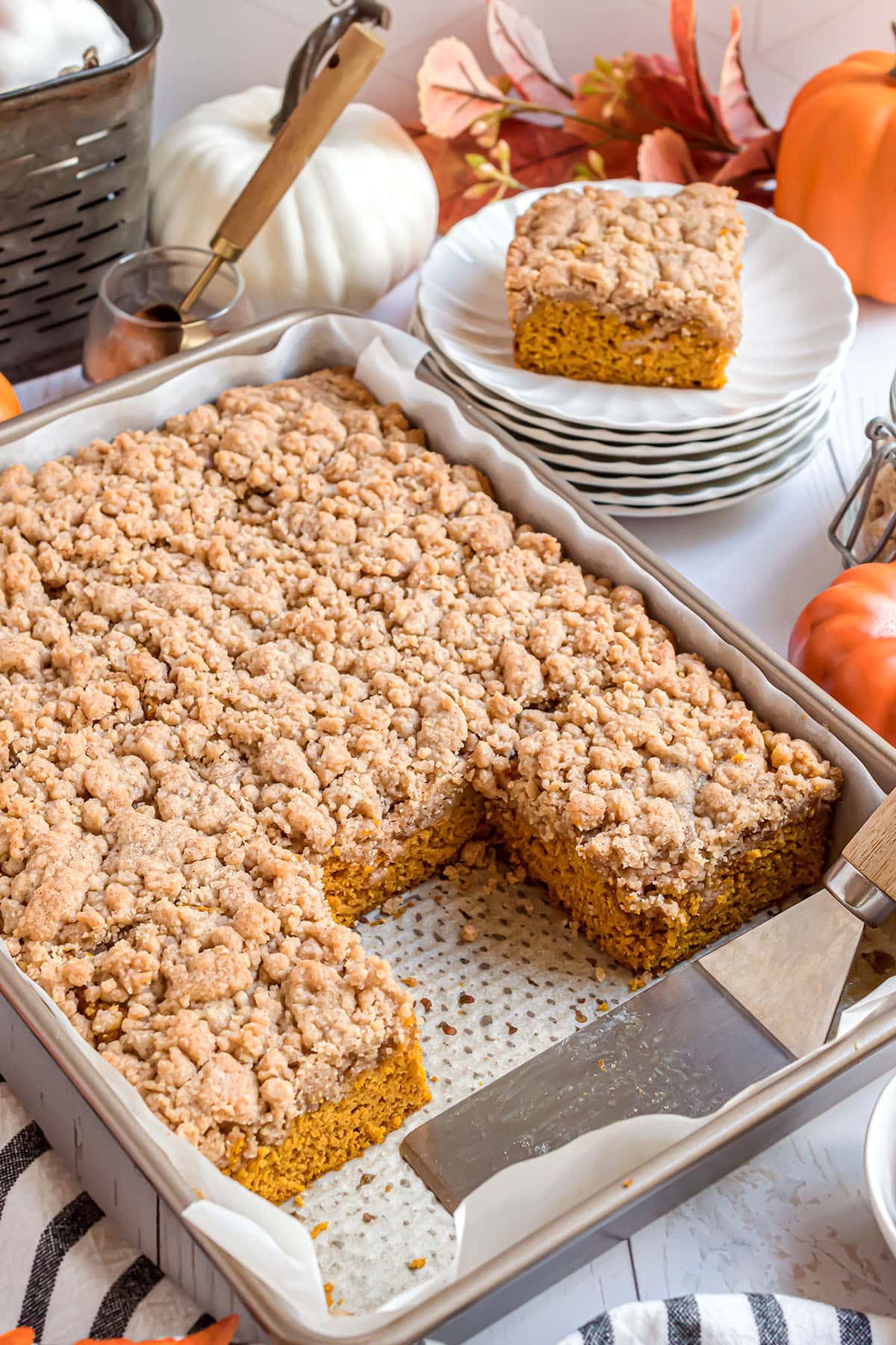 Baked pumpkin coffee cake with crumb topping in a cake pan with a few servings on plates