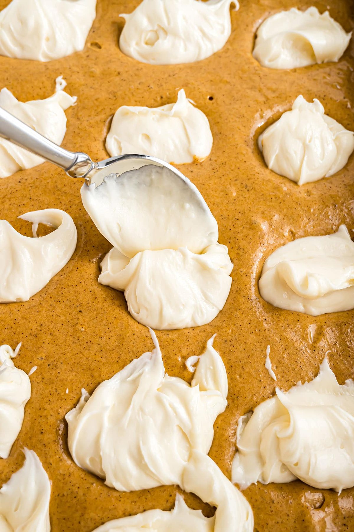 Cream cheese frosting being dolloped onto a pumpkin cake.