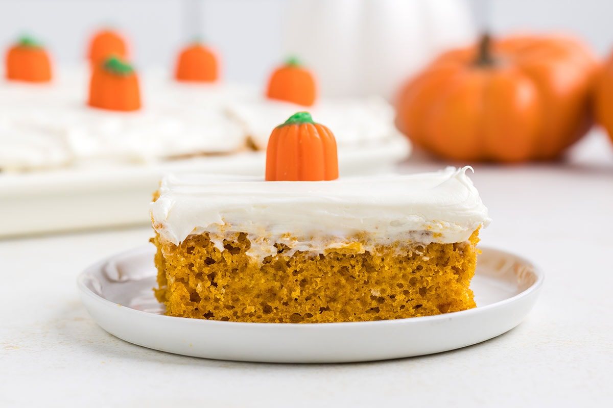 serving of fall cake with white frosting on a white plate and topped with pumpkin candy