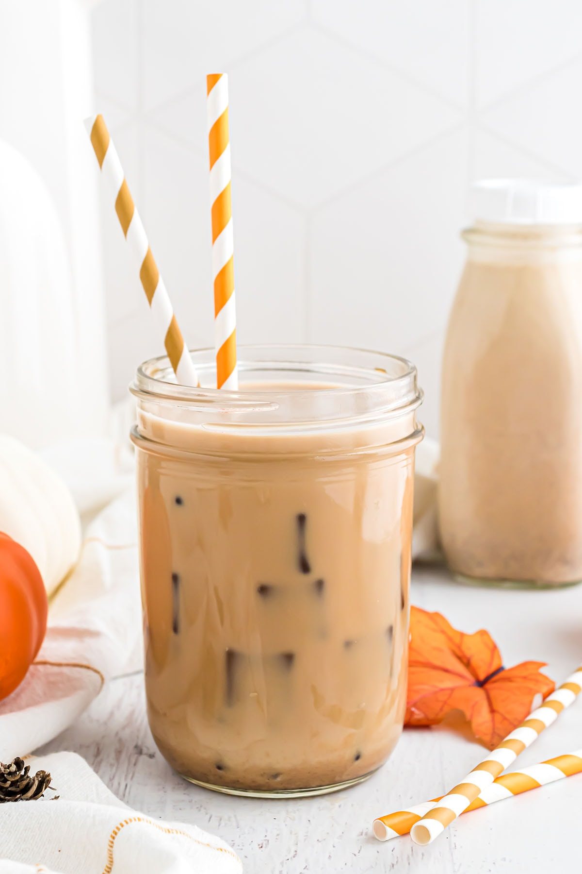 a glass of iced coffee with homemade pumpkin spice creamer and orange striped straws.