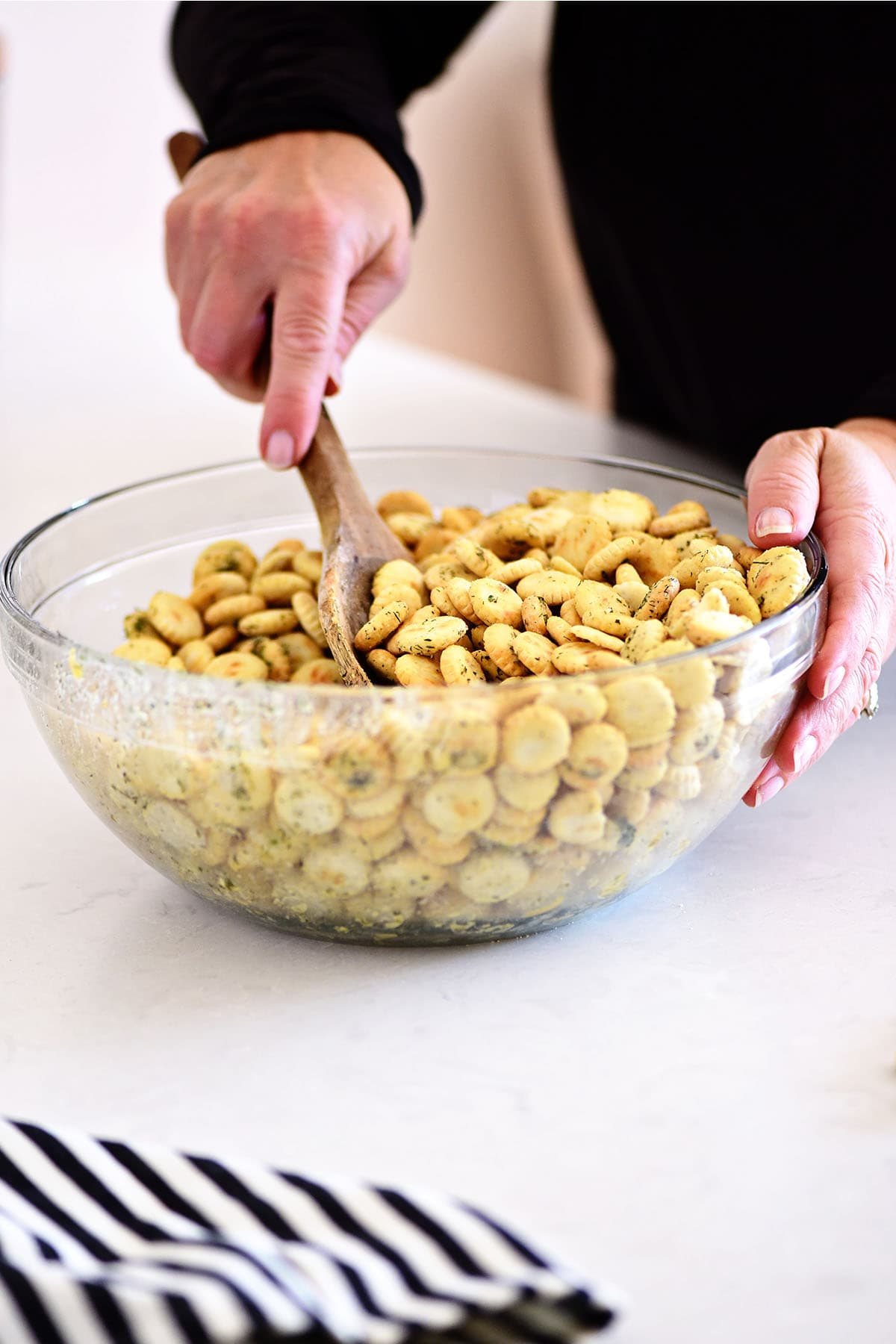 mixing seasoned oyster crackers in a glass bowl with a wooden spoon