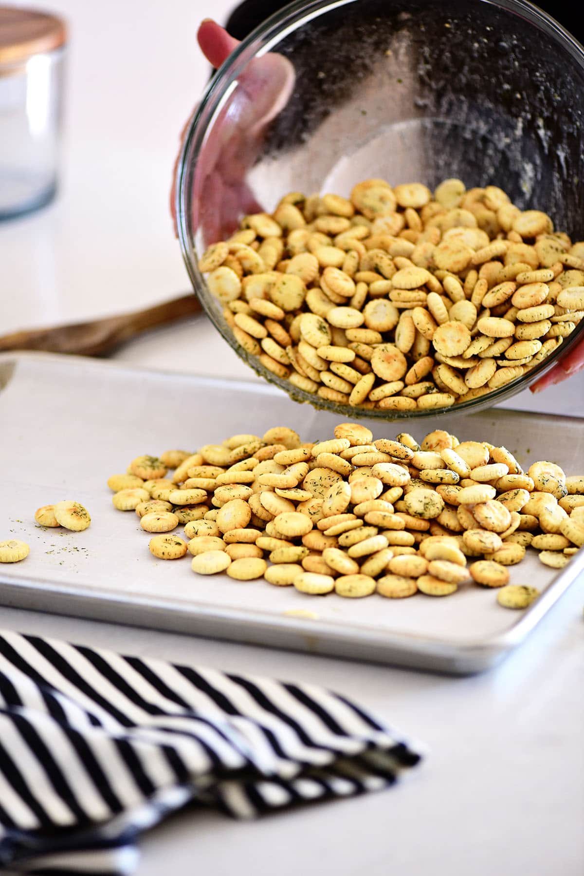 pouring oyster crackers onto a pan to bake in the oven