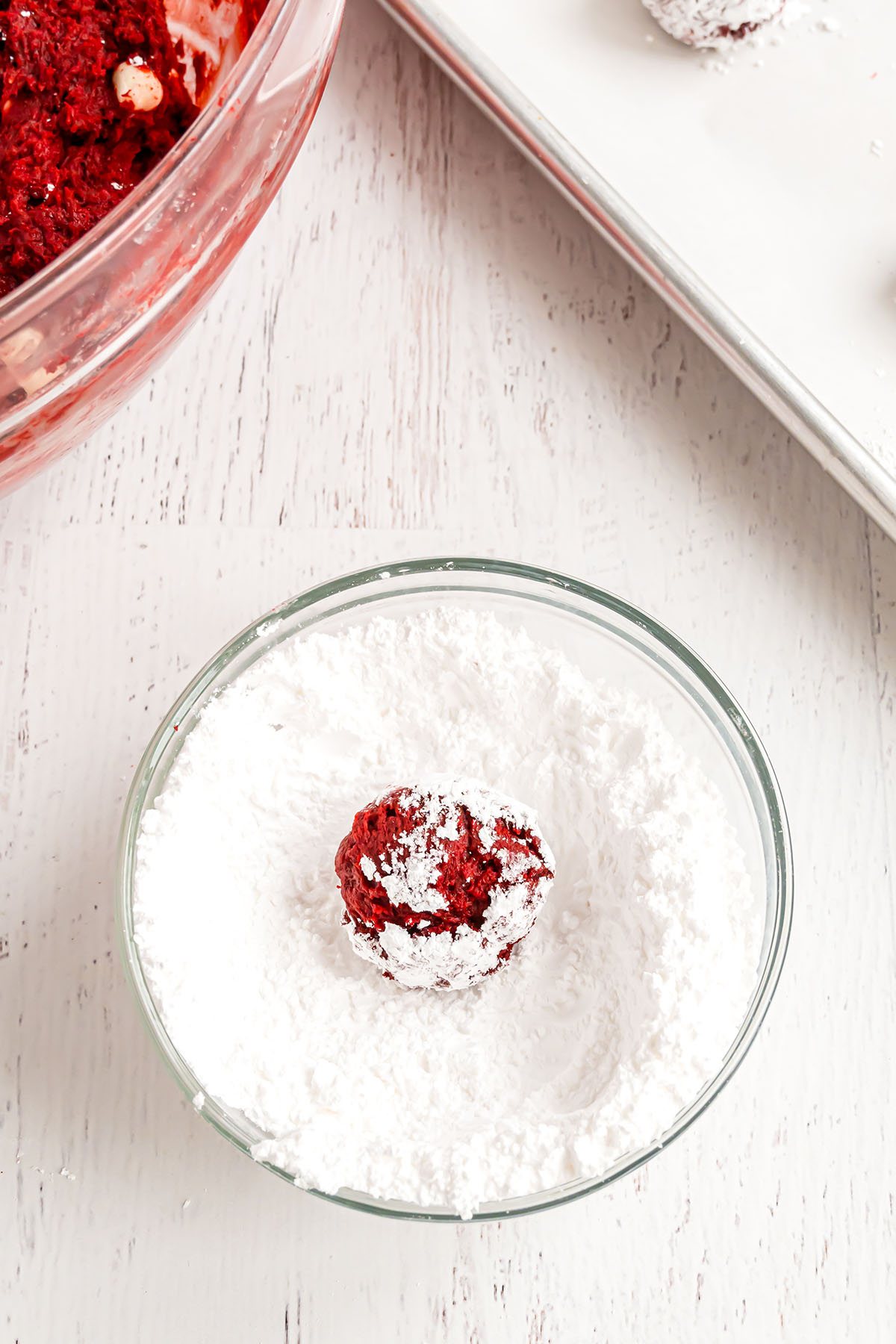rolling a red velvet cookie dough ball in powdered sugar