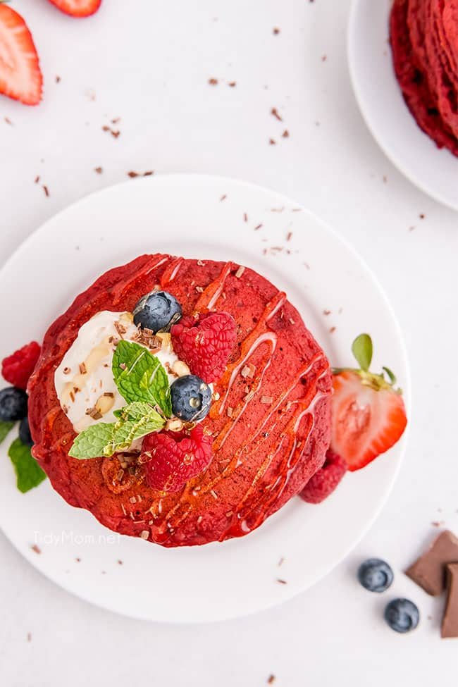 a stack of red velvet pancakes with fruit on and around the stack