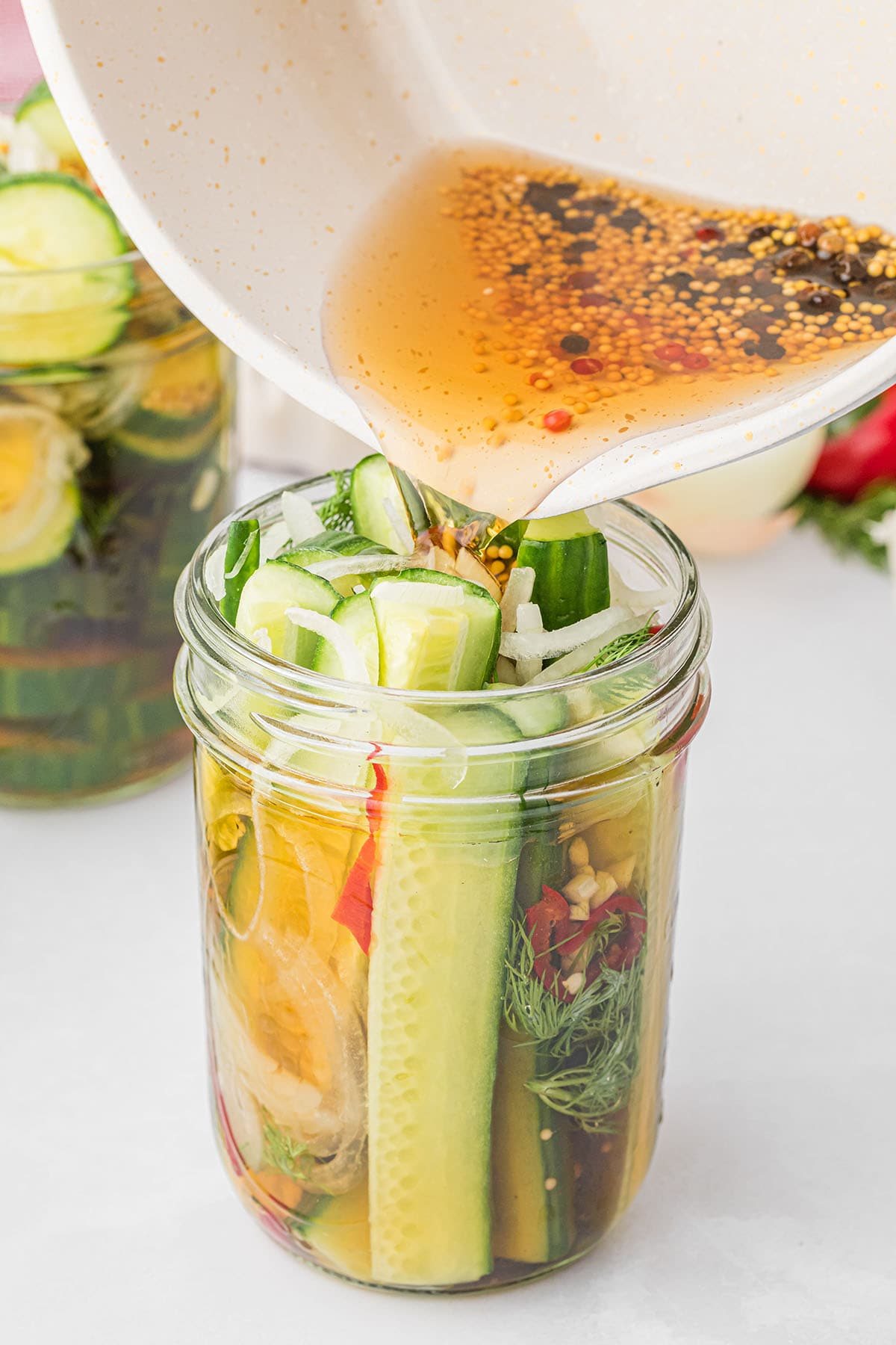 pouring brine over a jar of cucumber spears