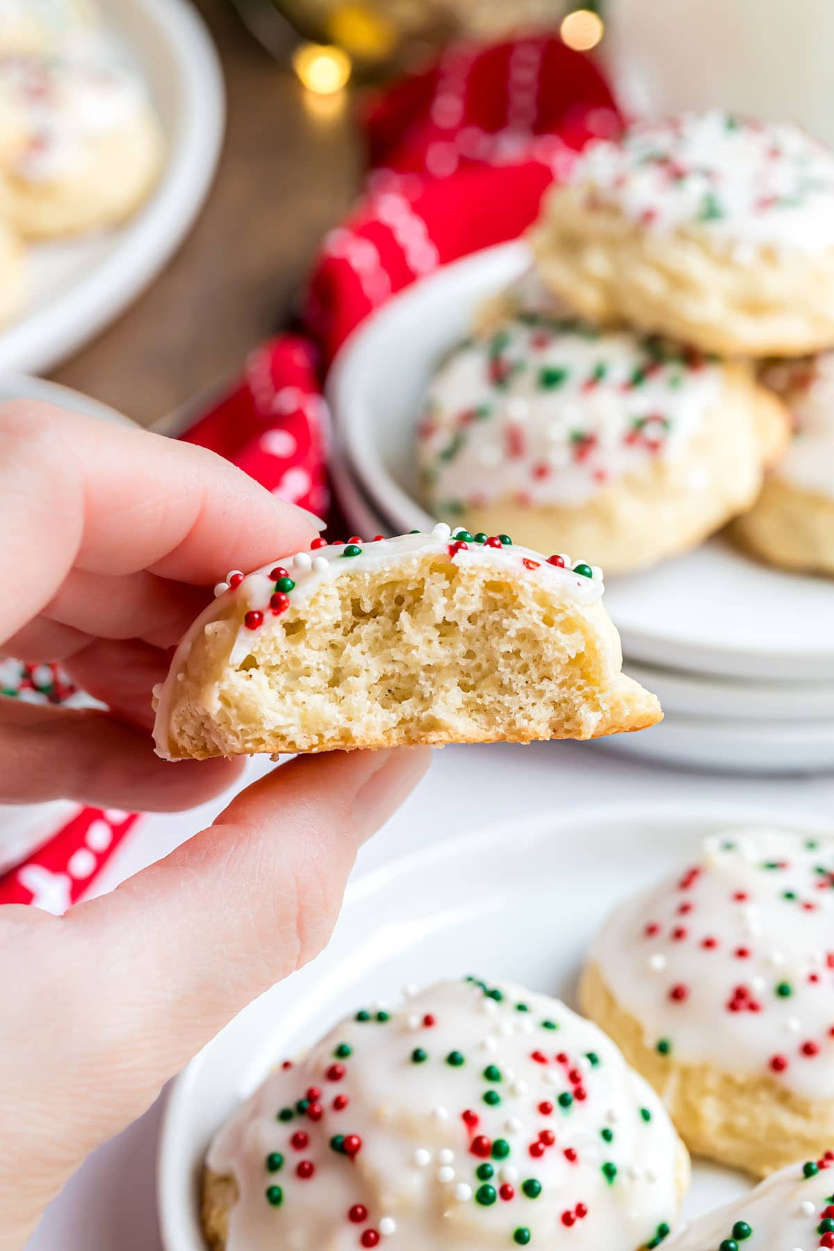 a woman's hand holding a ricotta cookie with a bite missing.