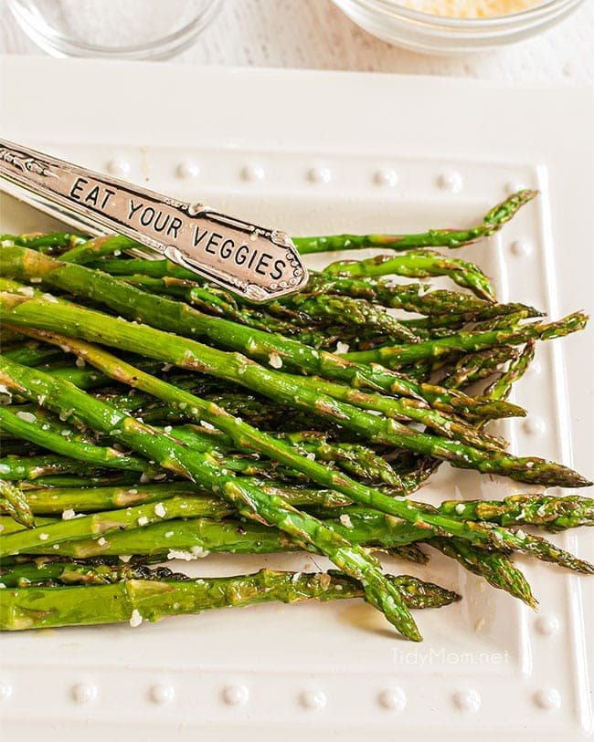 baked asparagus on a plate with tongs that says "eat your vegetables"