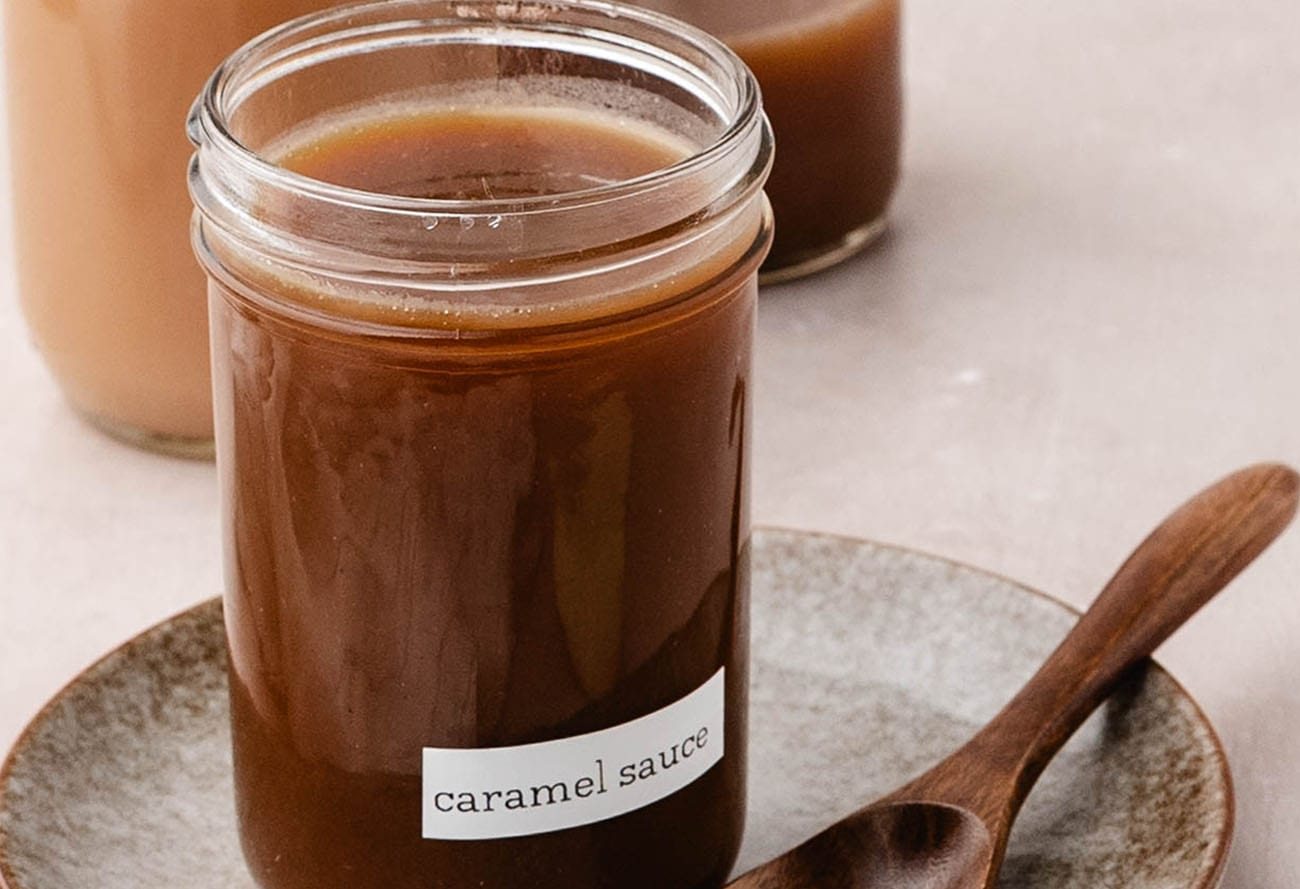 Homemade apple cider caramel sauce in a glass jar with a wooden spoon.