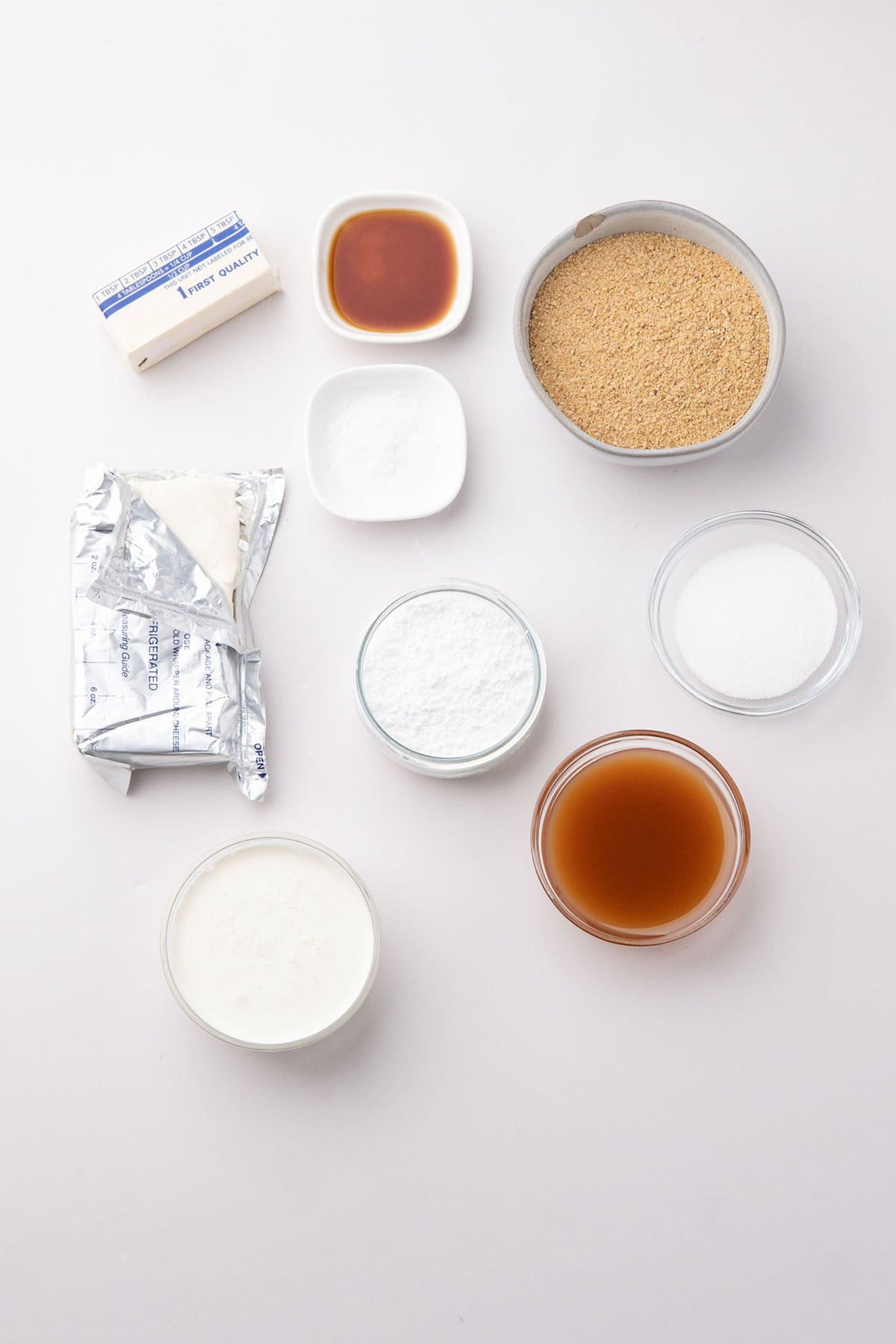 Cream cheese, heavy cream, graham crackers, sugar, vanilla, and caramel sauce arranged for the recipe.
