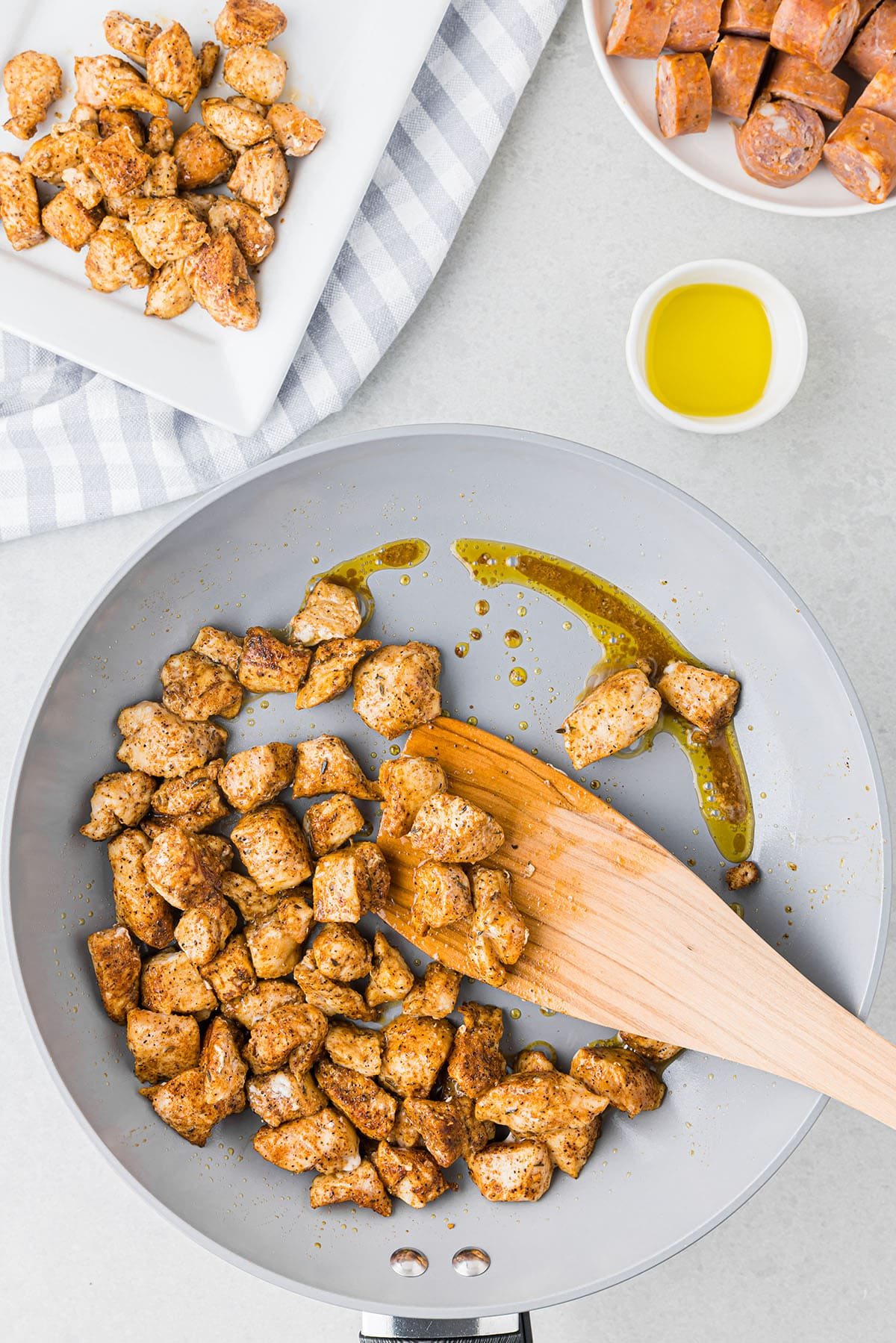seasoned chicken pieces in a skillet with a wooden spatula