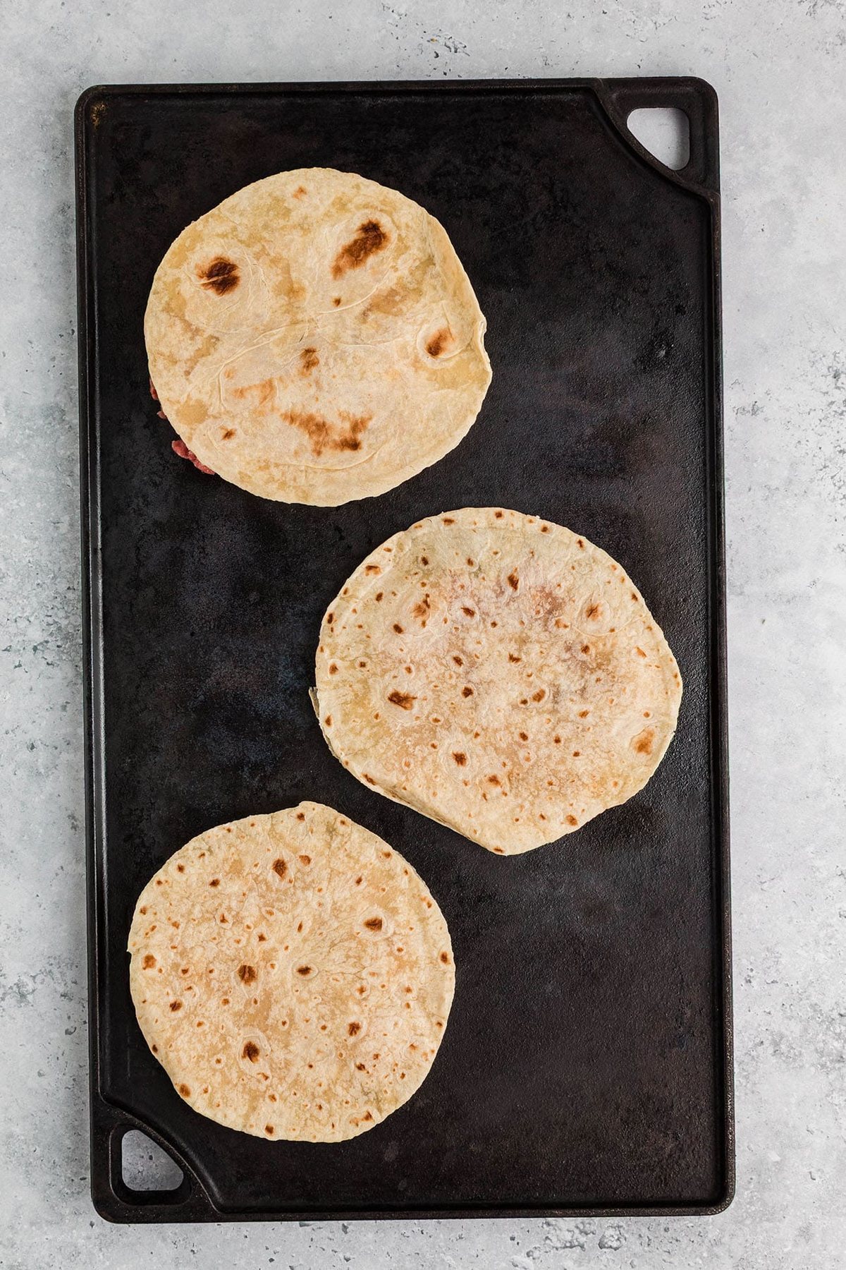 Flour tortillas on a skillet for Smash burger tacos