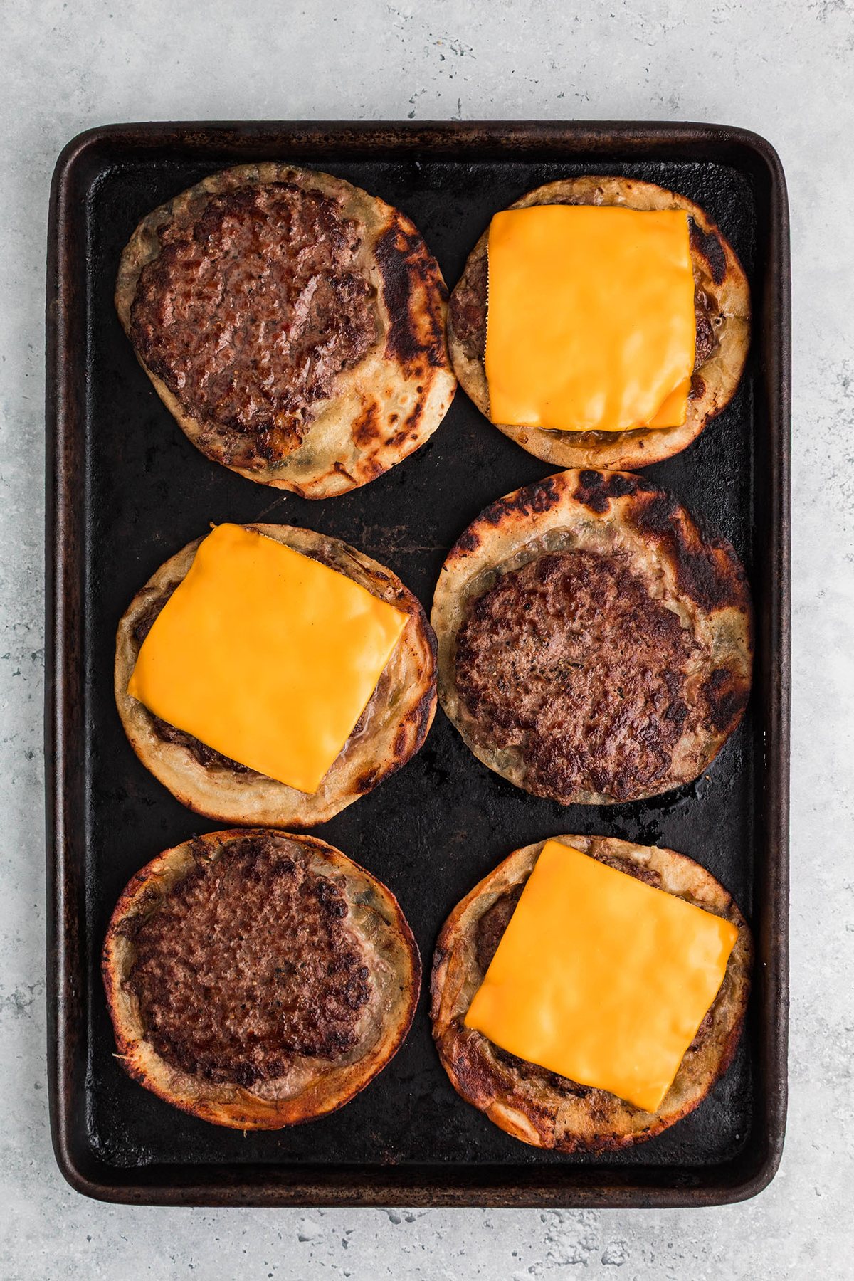 Smash burger tacos cooking in a skillet with beef pressed onto tortillas
