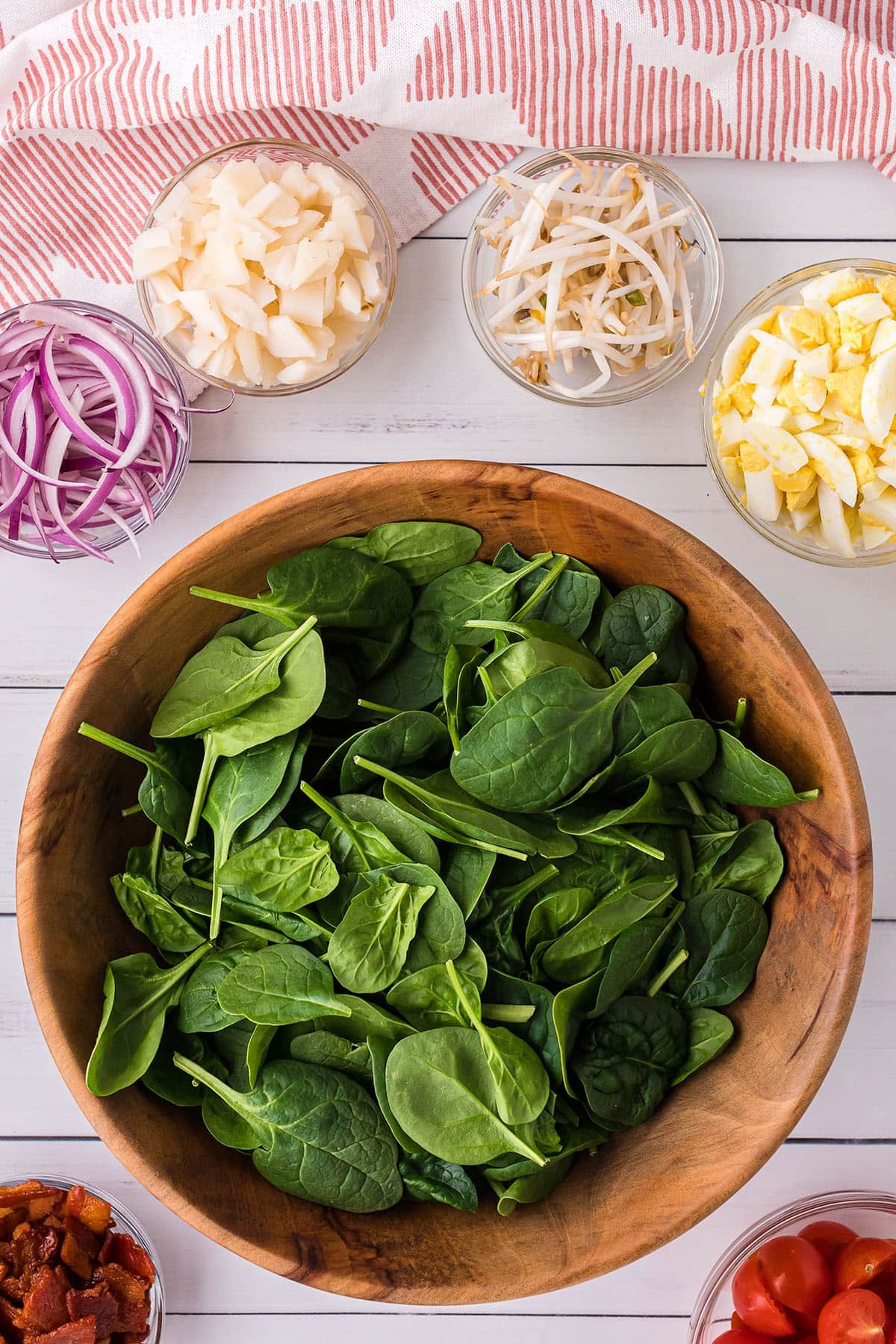a wood bowl with baby spinach and little glass bowls with onions, sprouts, water chestnuts and diced hard-boiled eggs