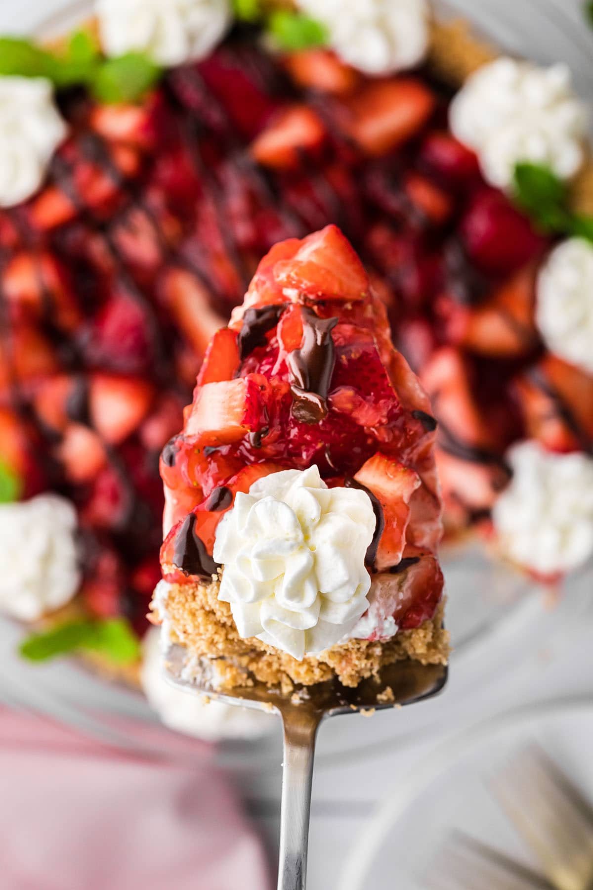 piece of fresh strawberry pie with whipped cream on a pie server over a full pie