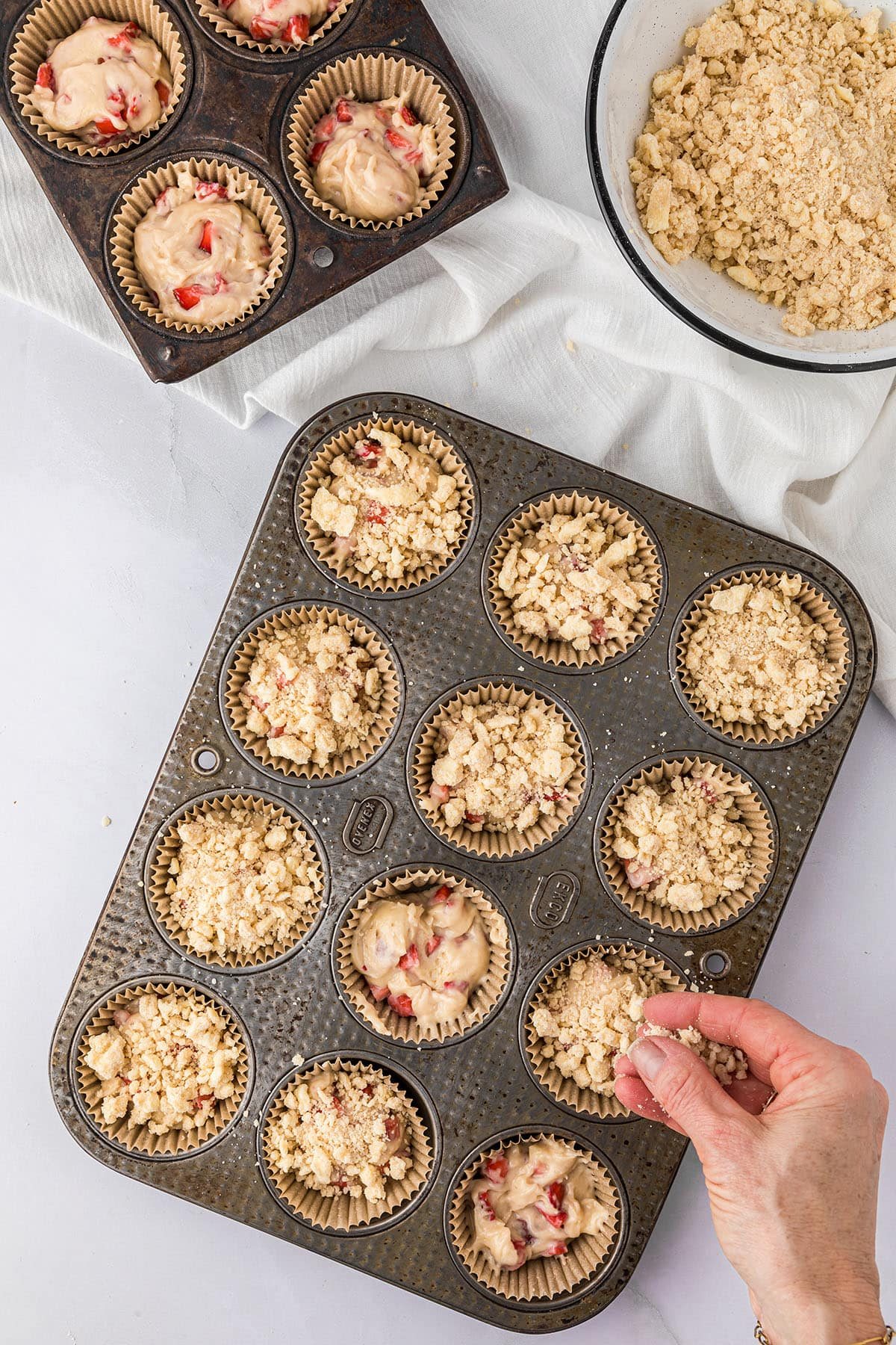 putting crumb topping on muffins in a pan