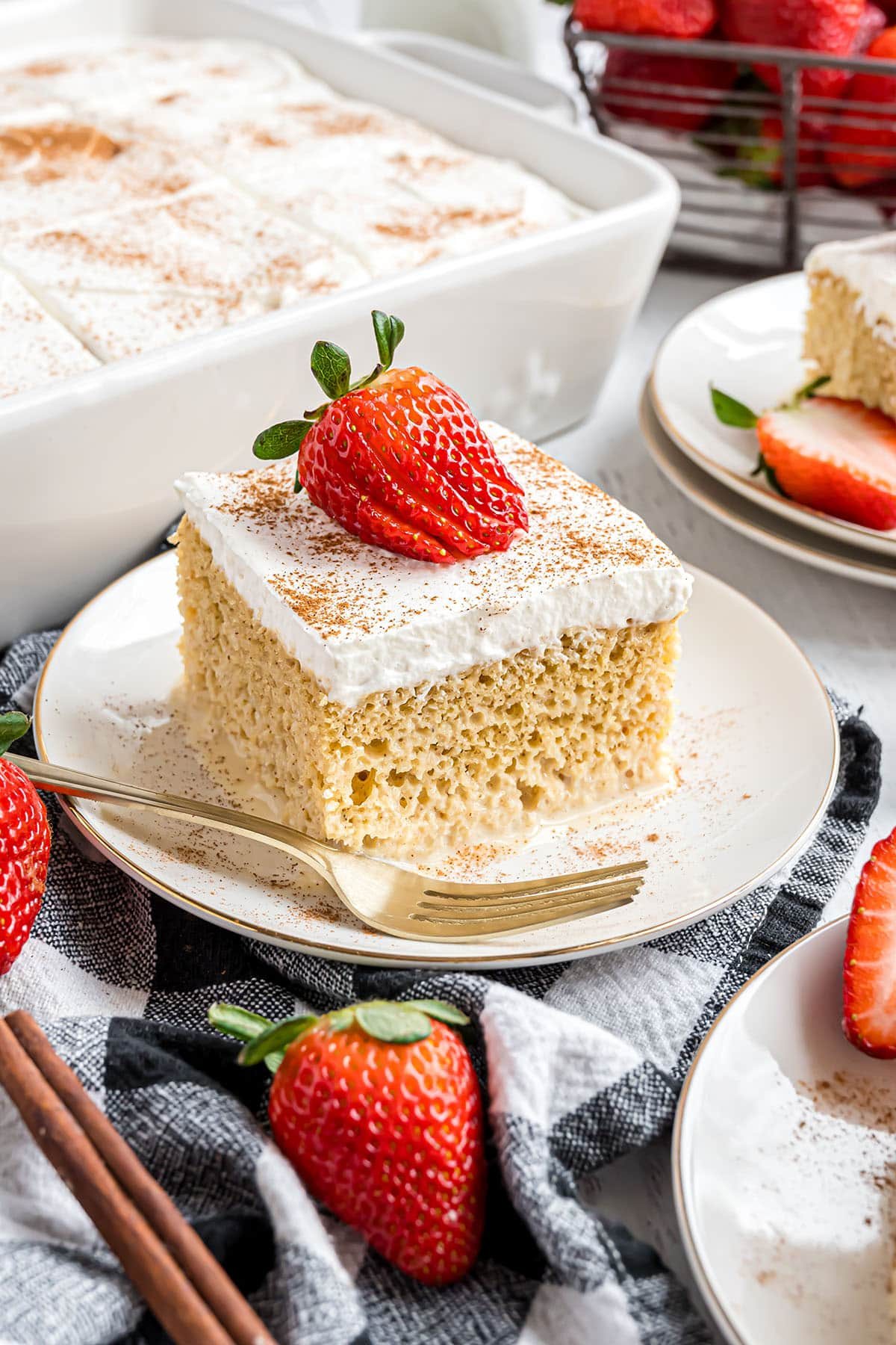 moist tres leches cake with a fresh strawberry and a fork on a white plate
