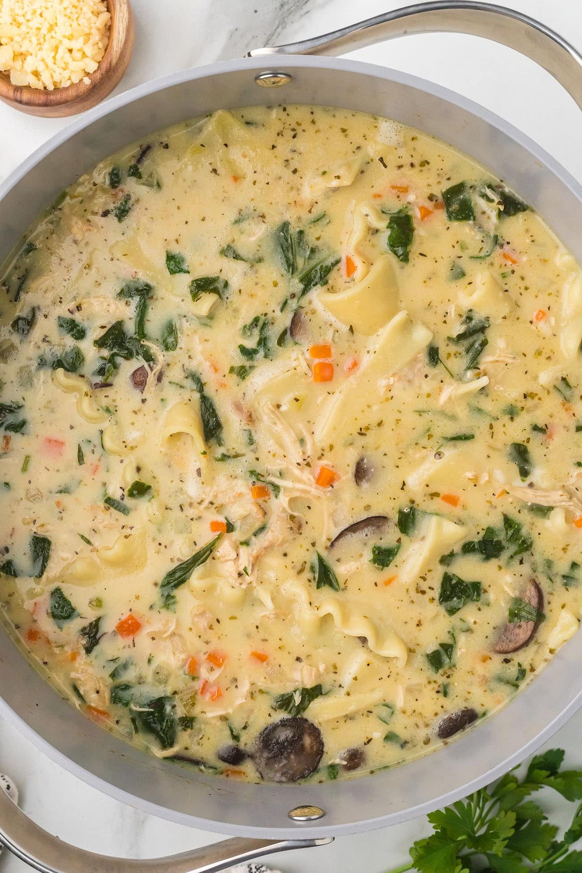 large soup pot full of white lasagna soup including rotisserie chicken, vegetables, broth, coconut milk, pasta, and cheese.
