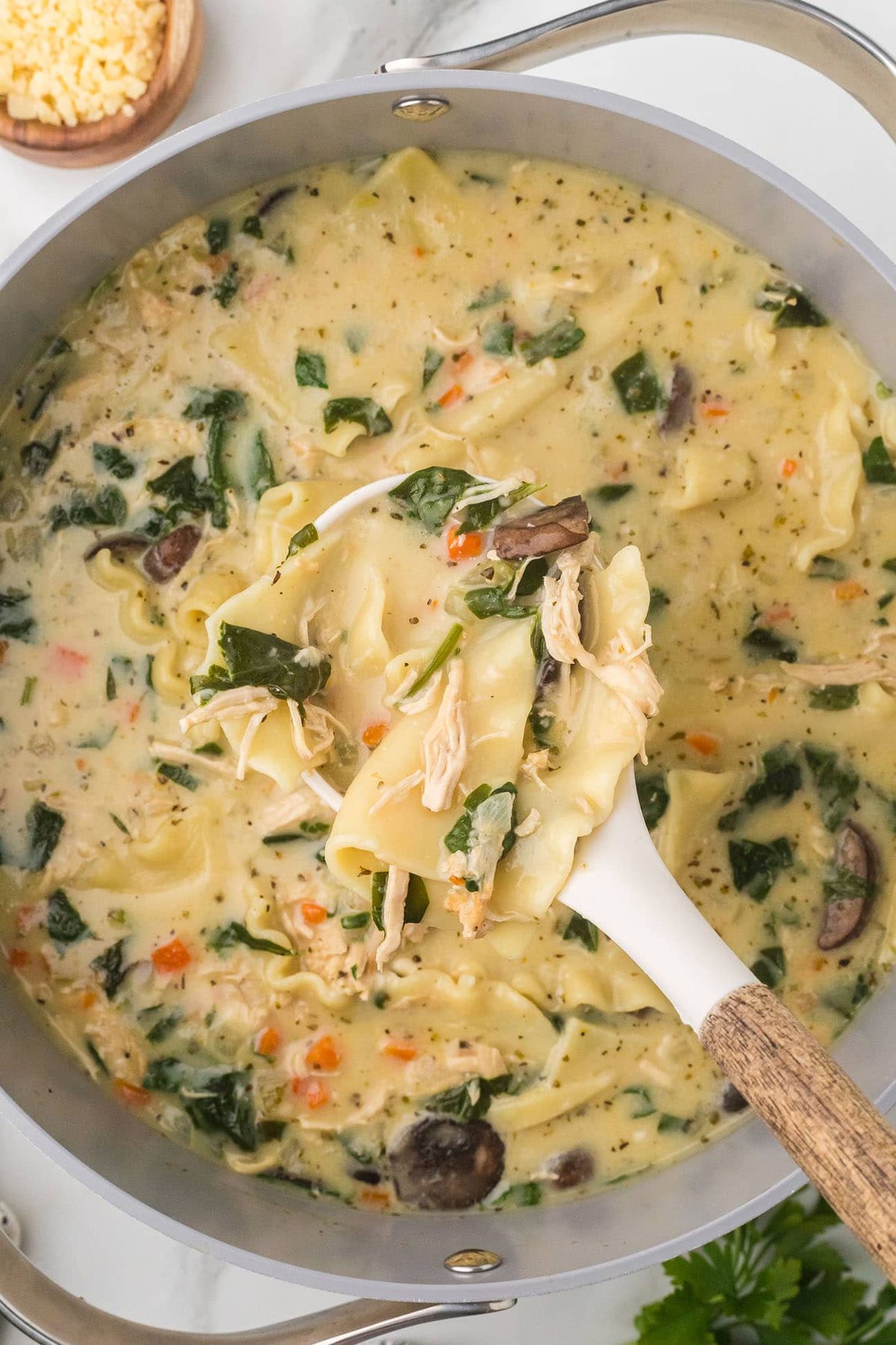 large pot and spoon full of white lasagna soup including rotisserie chicken, vegetables, broth, coconut milk, pasta, and cheese.