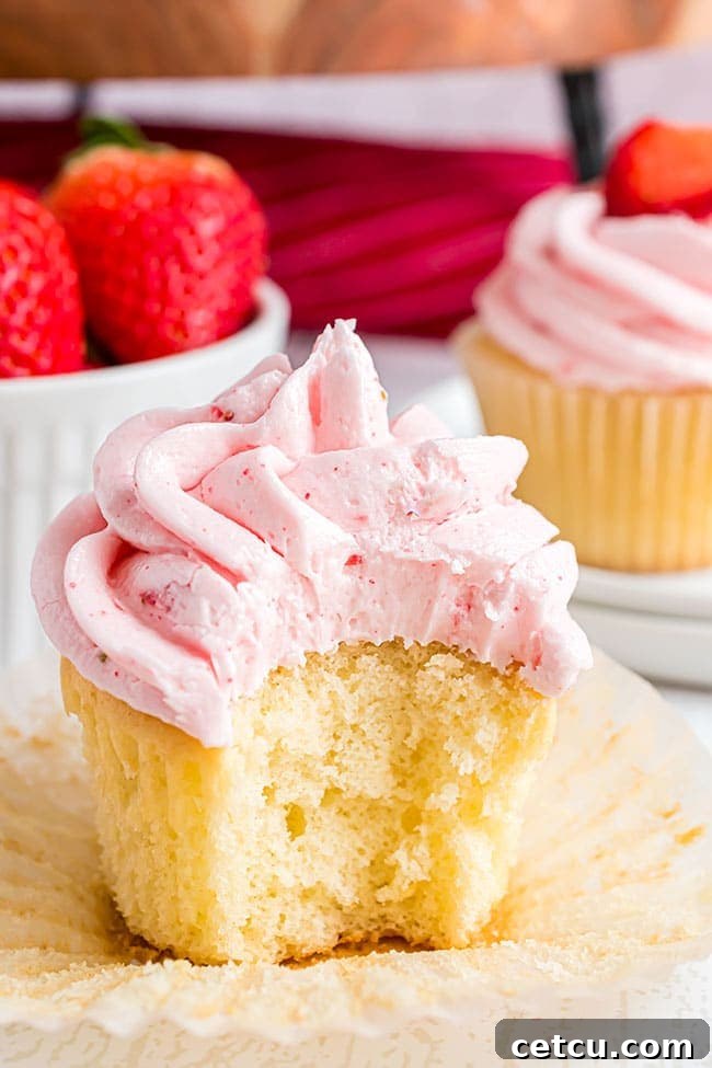 a bite taken out of a vanilla cupcake with strawberry frosting and 