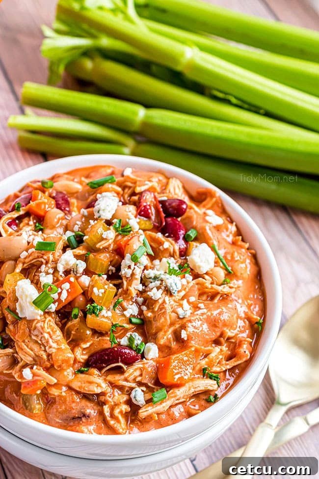 A close-up shot of a bowl of Buffalo Chicken Chili, perfectly garnished with blue cheese, green onions, and a side of fresh celery sticks, enhancing its vibrant appeal.