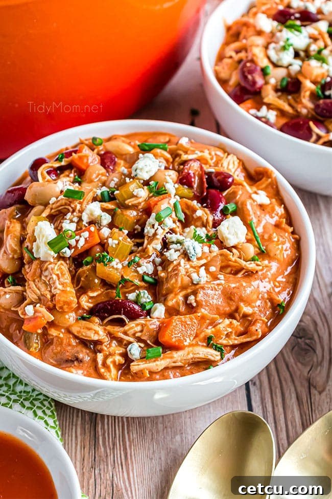 A large white bowl brimming with creamy Buffalo Chicken Chili, adorned with a swirl of sour cream, blue cheese crumbles, and fresh herbs, ready for a comforting meal.