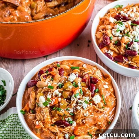 Two bowls of buffalo chicken chili, richly garnished with blue cheese crumbles and green onions, set against a warm, inviting backdrop.