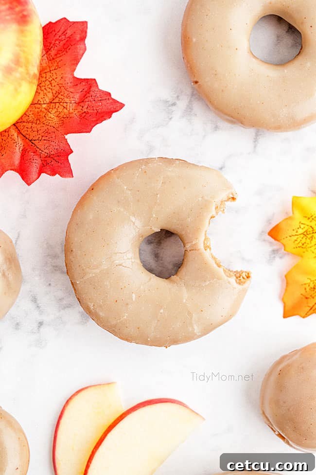 Freshly baked apple cider donuts glistening with brown butter glaze, artfully arranged on a pristine white counter, evoking a sense of cozy autumn baking