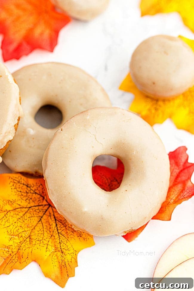 A festive arrangement of glazed apple cider donuts nestled among vibrant colorful fall leaves, capturing the essence of autumn