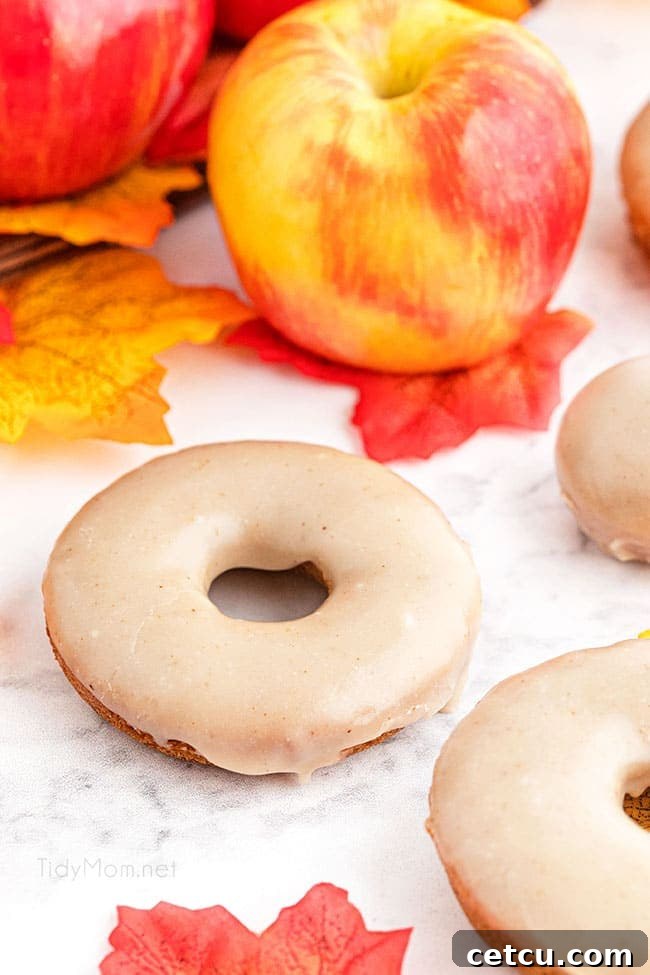 A charming fall display featuring glazed apple cider donuts alongside a rustic basket brimming with fresh apples and colorful autumn leaves