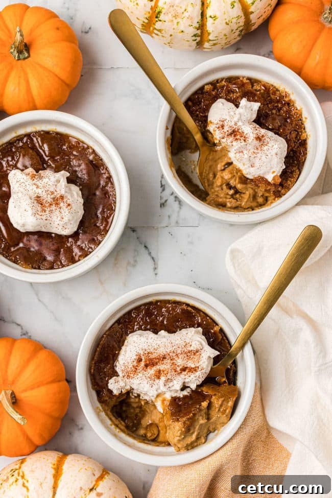 Three elegant servings of Pumpkin Crème Brûlée, each with a golden spoon, arranged beautifully on a textured surface, showcasing their inviting caramel crusts.