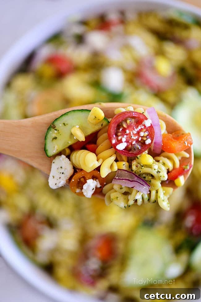 Sunshine Pasta Salad 6 Overhead shot of summer pasta salad being scooped from a white bowl with a serving spoon.
