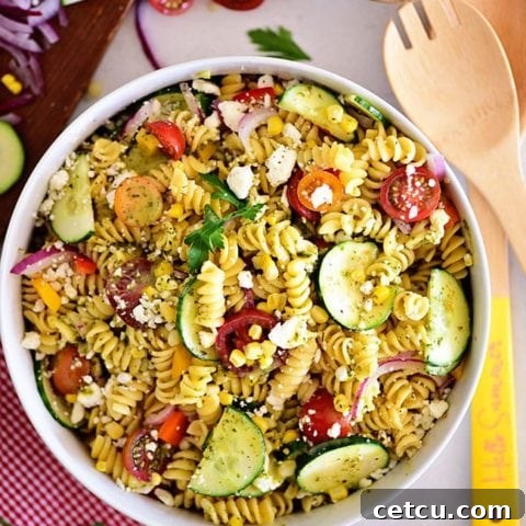 Overhead shot of a colorful summer pasta salad in a white bowl, garnished with fresh herbs.