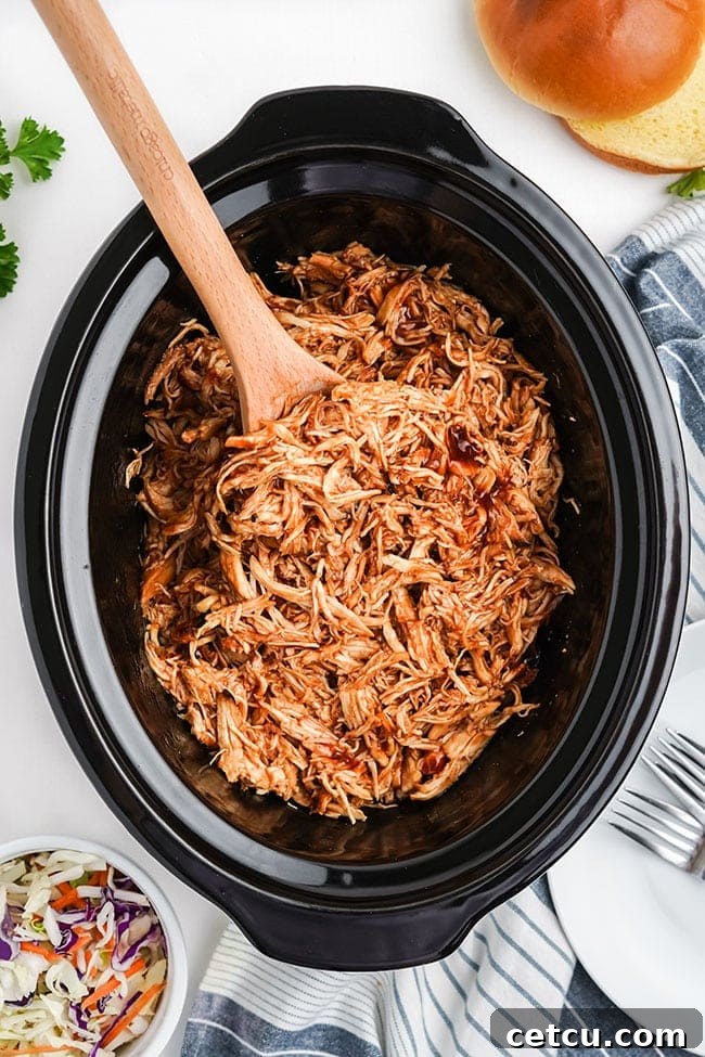 Close-up of boneless, skinless chicken breasts submerged in barbecue sauce within a slow cooker