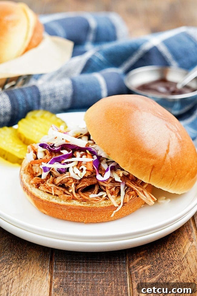 An opened slow cooker pulled chicken sandwich with soft bun and melted cheese, showcasing the tender chicken