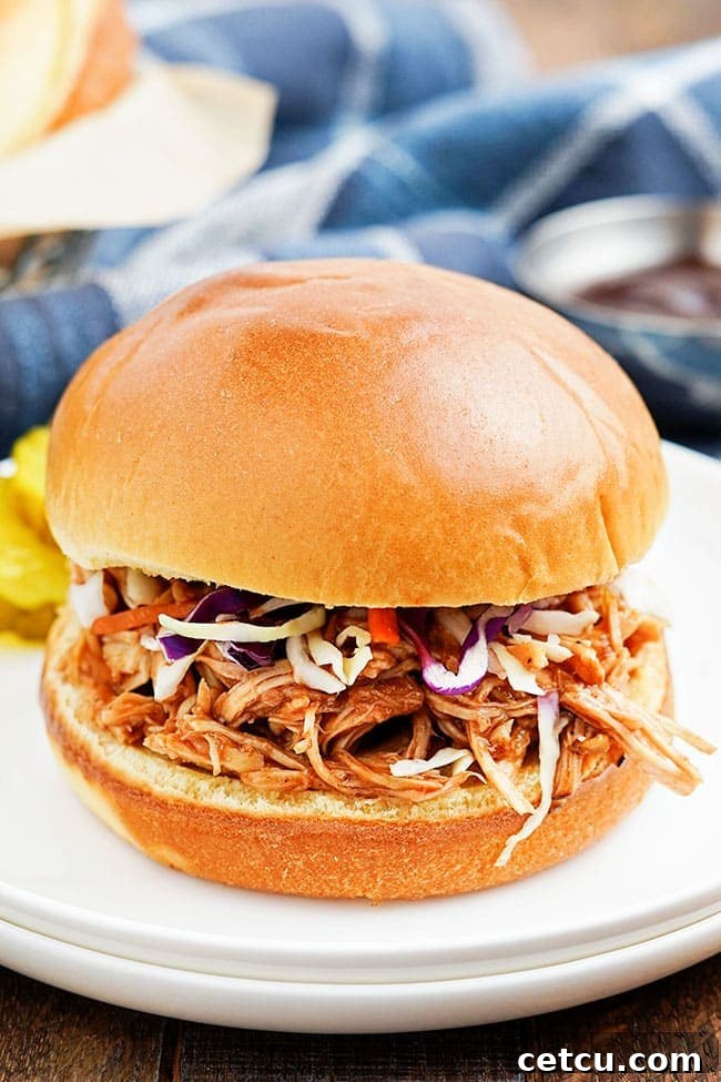 Two Slow Cooker Pulled BBQ Chicken Sandwiches topped with fresh coleslaw, served on a white plate
