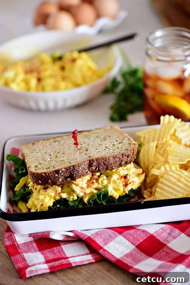 A classic egg salad sandwich presented on a tray with a side of crispy chips.
