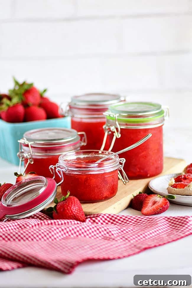 Several jars of homemade strawberry freezer jam with fresh berries displayed beautifully