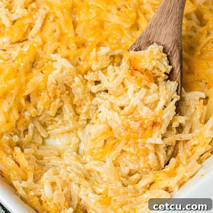close up of cheesy hashbrown casserole in a baking dish with a wooden spoon
