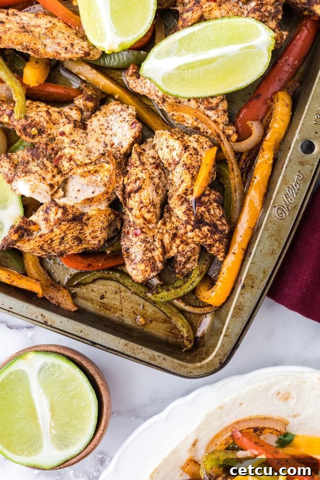 Juicy sheet pan chicken fajitas with colorful bell peppers and limes, ready to serve in warm tortillas.