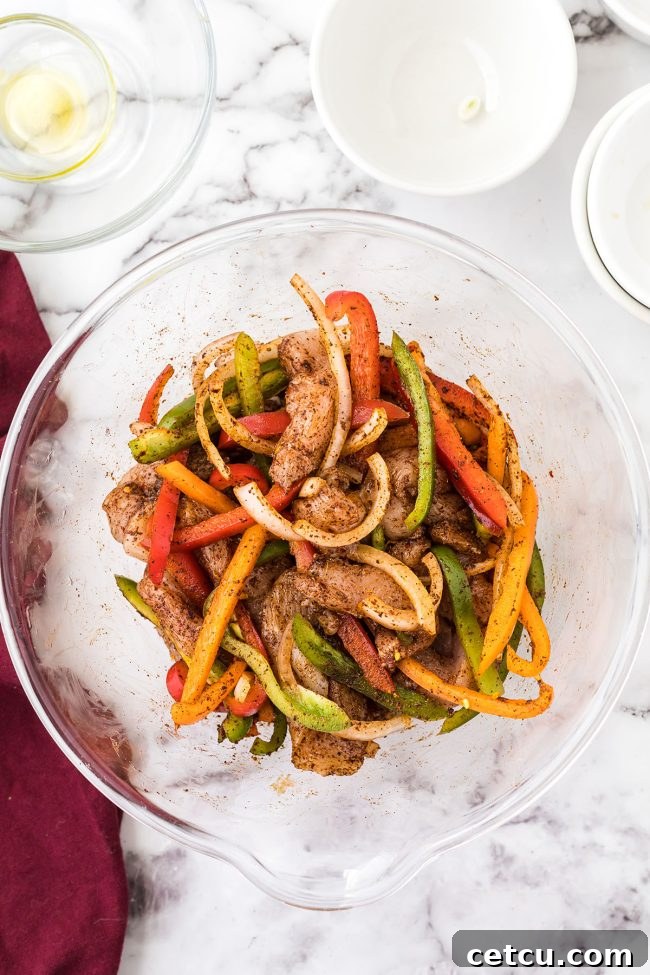 Chicken and vegetables mixed with fajita seasonings in a glass bowl.