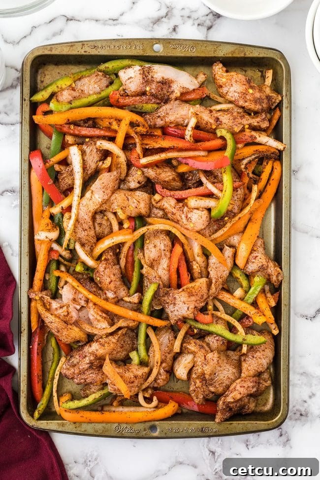 Chicken and seasoned vegetables spread evenly on a sheet pan before baking.