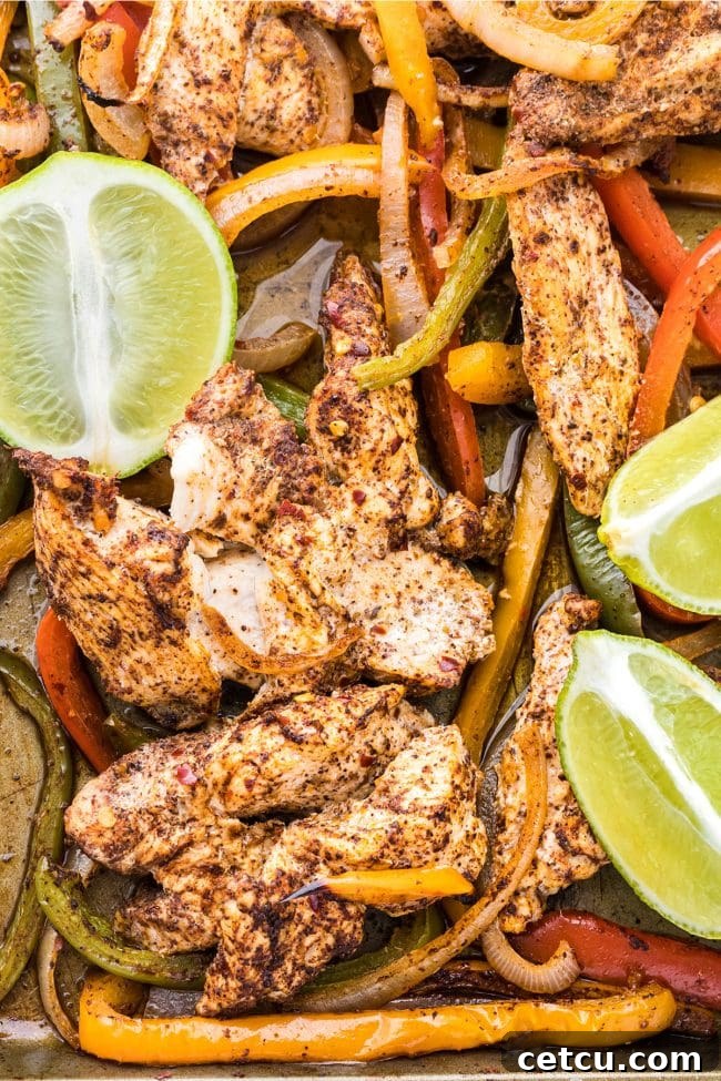 Close-up of oven-baked chicken fajitas with chicken and colorful bell peppers, garnished with fresh lime slices on a sheet pan.