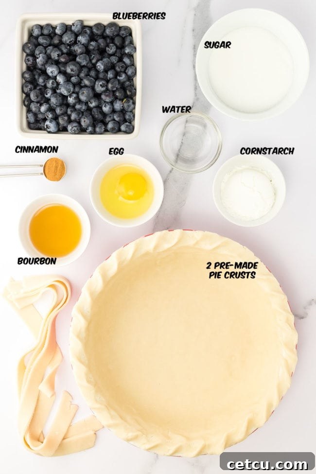 Arrangement of ingredients for homemade blueberry pie, including fresh blueberries, sugar, cornstarch, cinnamon, bourbon, and pie crusts.