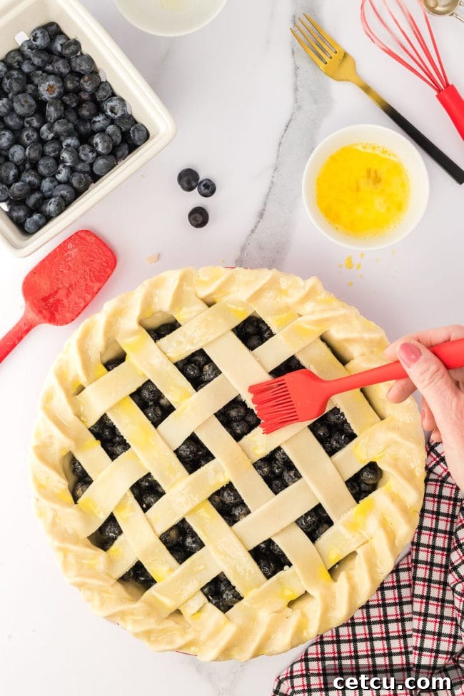 Step four: brushing an egg wash onto the lattice pie crust with a red pastry brush, giving it a golden sheen.
