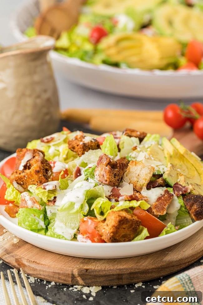 A large bowl filled with vibrant BLT salad, topped with crispy croutons and fresh avocado slices, ready to be served.