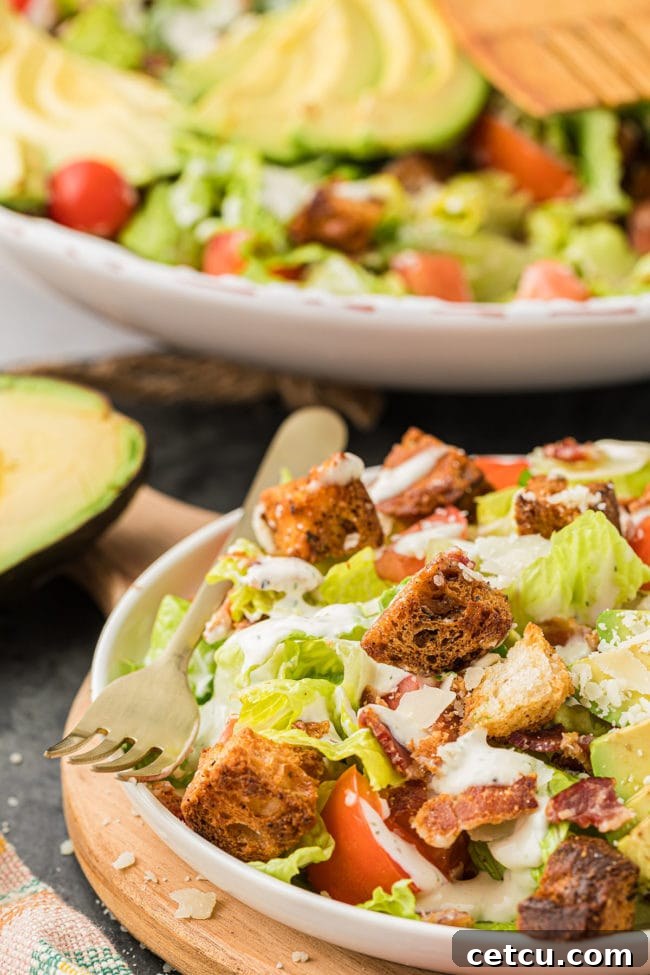 A vibrant BLT salad on a plate, with a fork ready to scoop, highlighting the freshness and appeal.